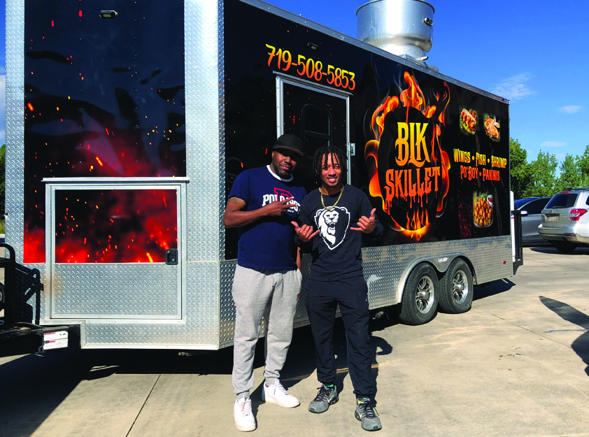 A food truck and it's two owners standing in front of it.